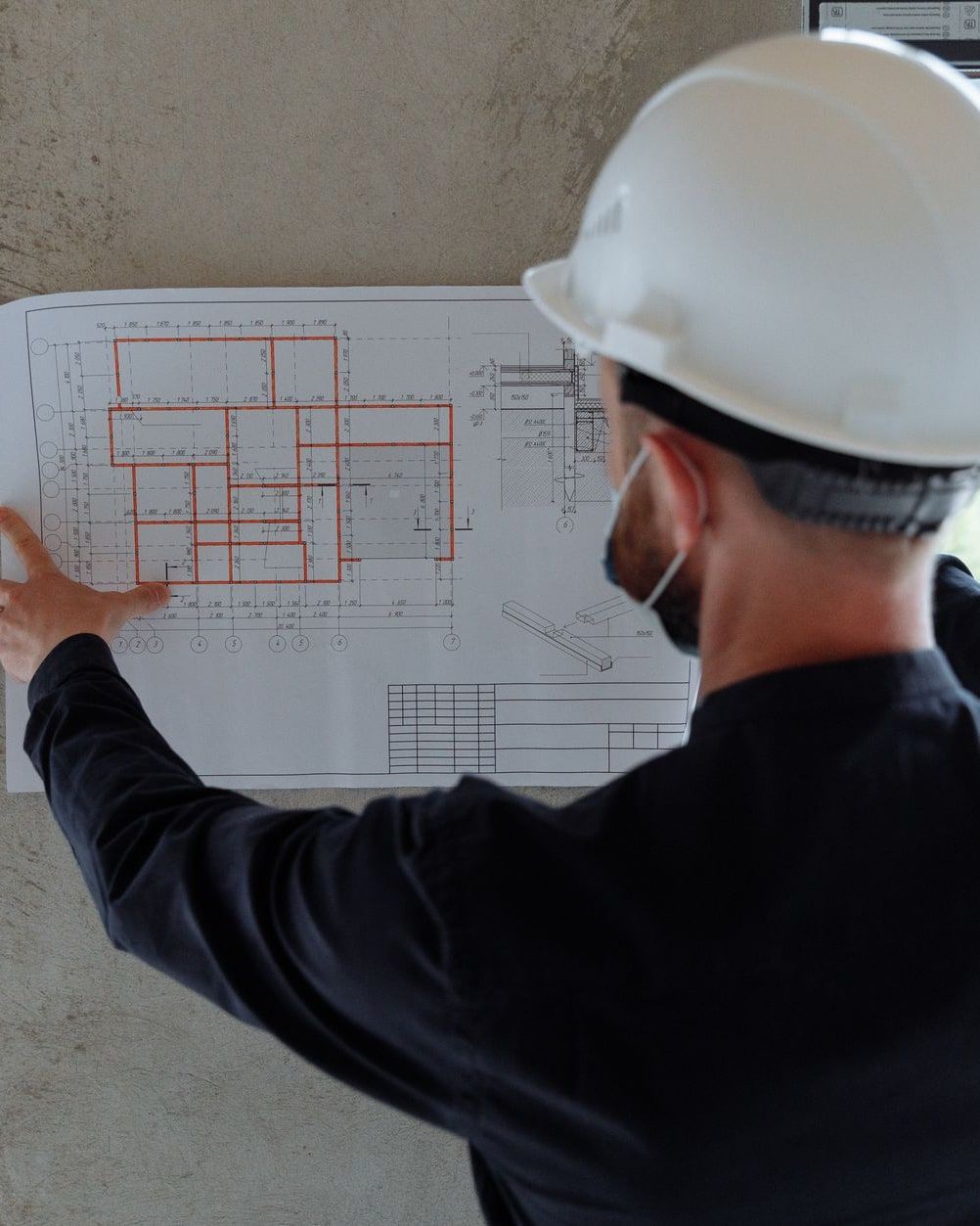 Bauingenieur mit Helm hält einen Plan vor einer fertigen Betonwand